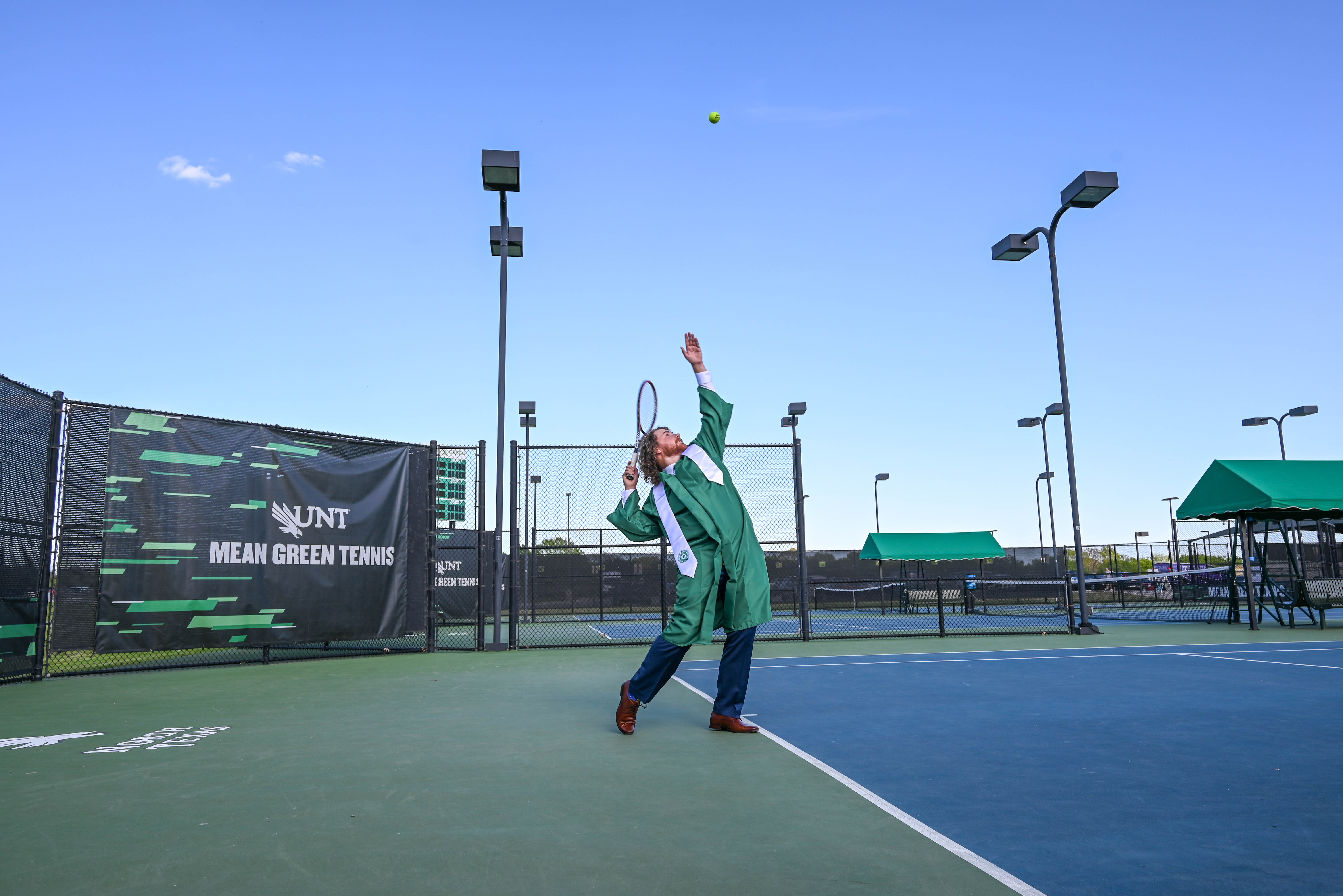 Bret serving a tennis ball in cap and gown.